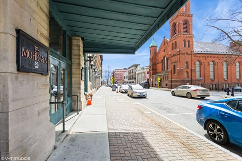 A street view with cars parked on the side and a building with a sign at Mohican Apartments, New London, CT