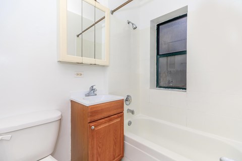 A white bathroom with a wooden cabinet and a white tub.