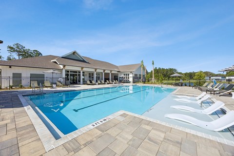 A large outdoor swimming pool with lounge chairs and a building in the background.