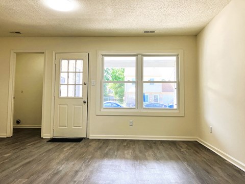 A room with a white door, a window, and a wooden floor.
