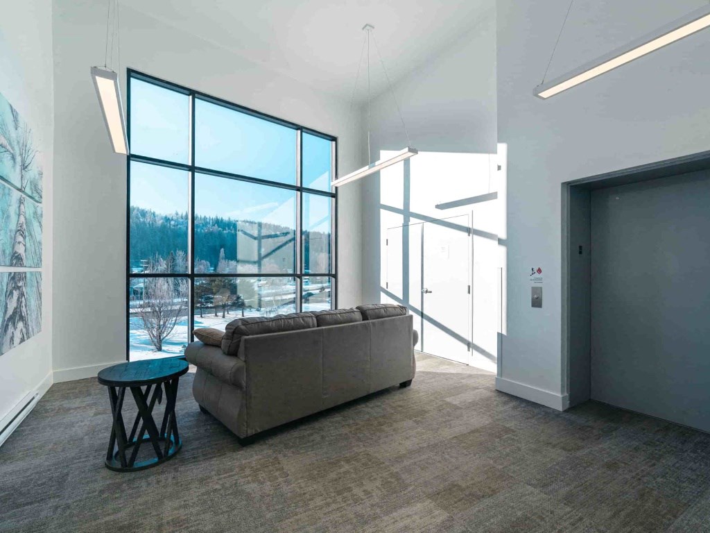 A room with a grey couch, a blue table and a large window.
