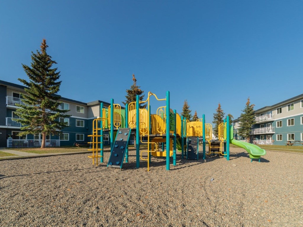 A playground with a yellow and green slide in the foreground.
