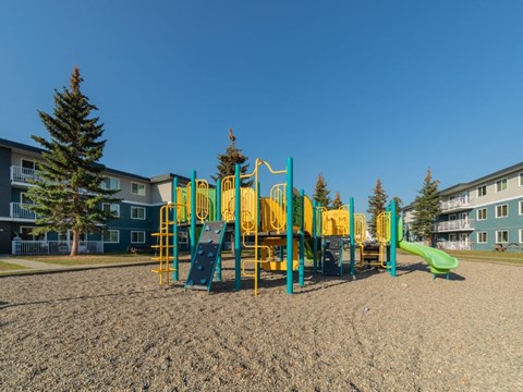 A playground with a yellow and green slide in the foreground.