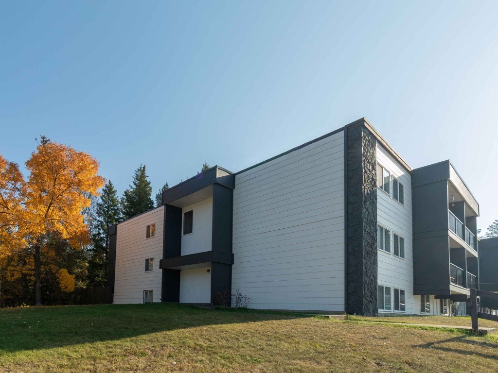 A modern building with a white and black facade is surrounded by a grassy area and trees.