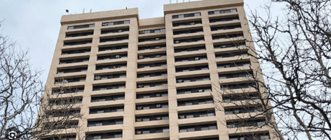 A tall building with many windows is surrounded by trees.