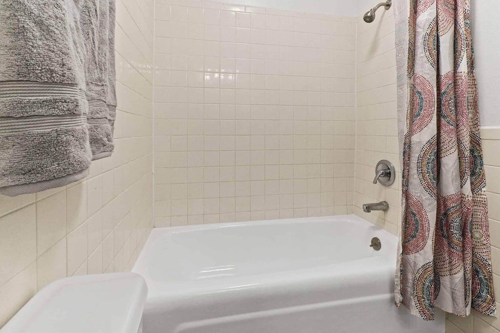 A white bathtub sits next to a toilet in a bathroom with white tiles.