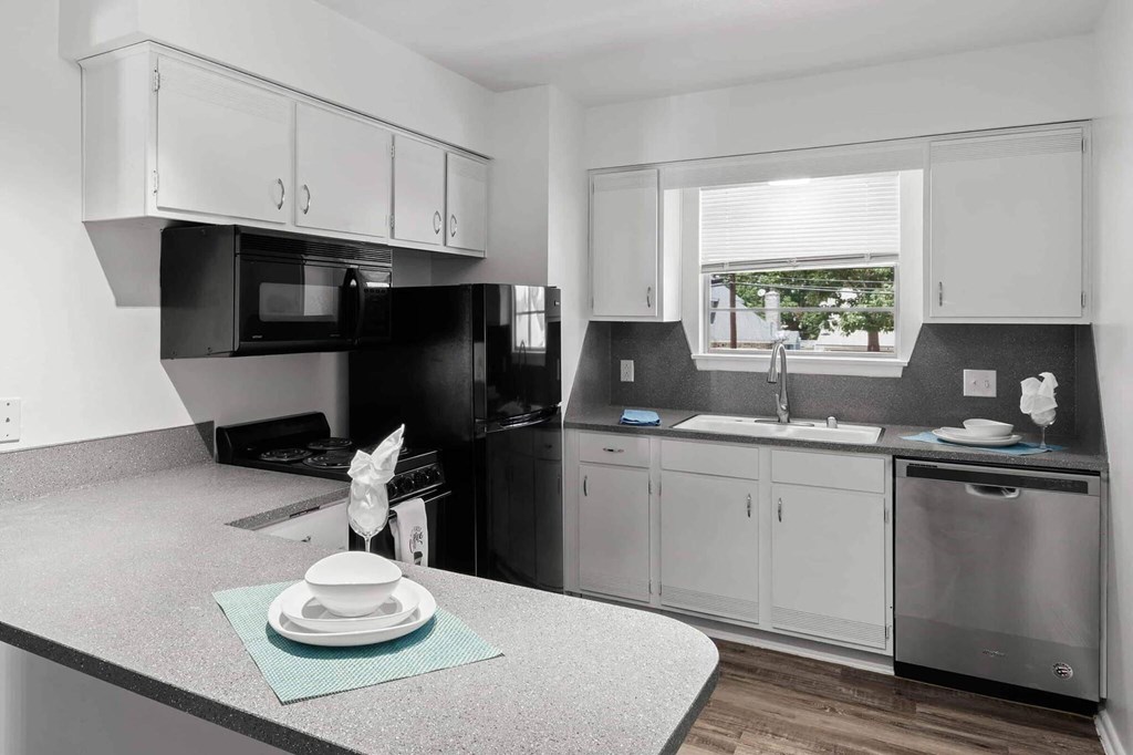 A kitchen with a black fridge and stove, white cabinets, and a window.