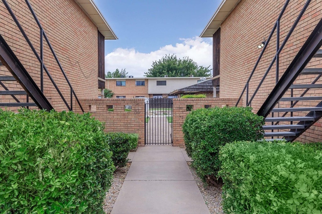 A brick building with a gate in the middle of a green hedge.