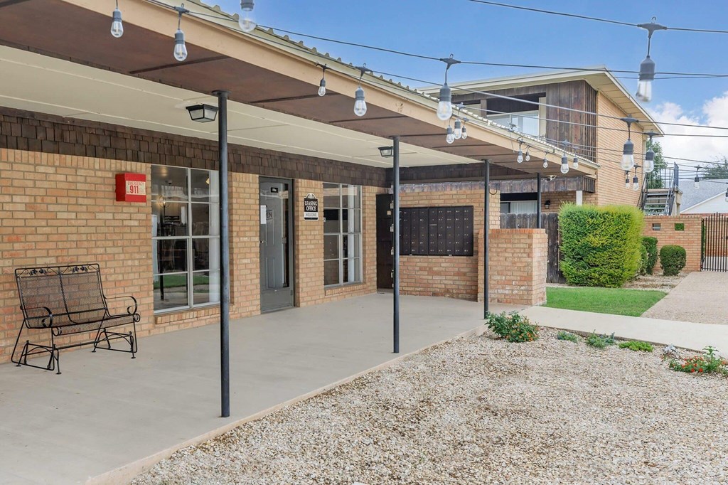 A building with a red sign on the left side and a bench under a canopy.