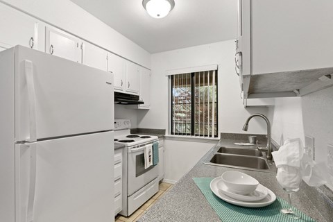 A white kitchen with a refrigerator, oven, and sink.