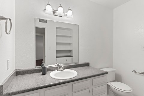 A bathroom with a sink, mirror, toilet and a towel ring on the wall.