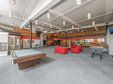 A billiard table is in the middle of a room with a pool table and a foosball table.