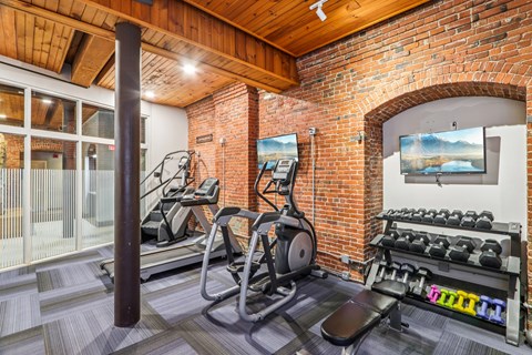 A gym with a brick wall and a row of treadmills.