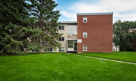 A red brick building with a white door and windows is surrounded by a green lawn.