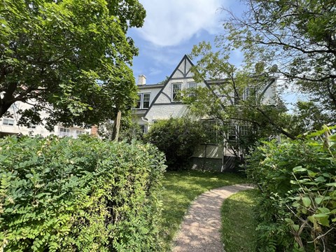 A pathway leads through a lush green garden to a house.