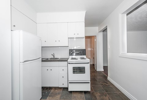 A white kitchen with a refrigerator, sink, and stove.