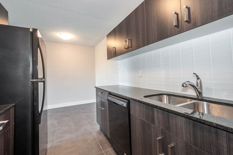 A kitchen with a black refrigerator and a stainless steel sink.