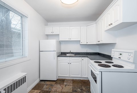 A white kitchen with a stove, sink, and cabinets.
