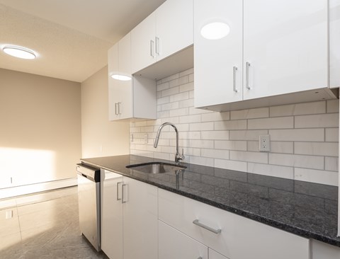 A kitchen with white cabinets and black countertops.