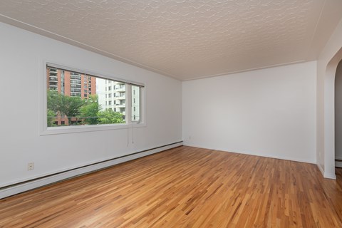 A room with wooden floors and a window showing a view of a building outside.