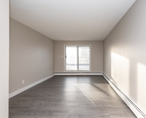 A spacious room with a window and wooden flooring.