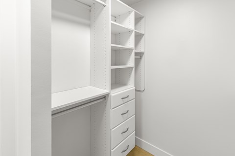 A white shelving unit with drawers is in a room with white walls.