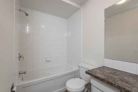 A white bathroom with a toilet, tub, and marble counter.