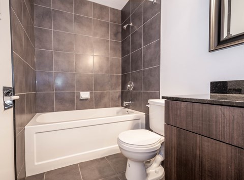 A white toilet sits next to a bathtub in a bathroom with brown tiles.