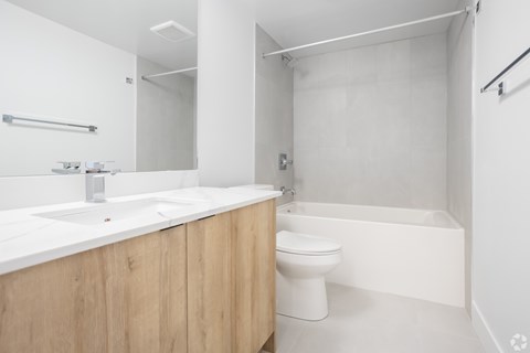 A white bathroom with a wooden vanity and a white toilet.
