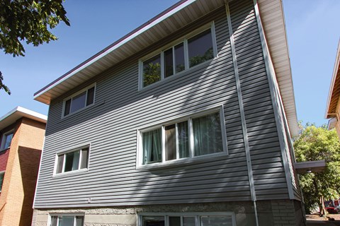 A grey house with a red brick building behind it.