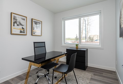 A black desk with a laptop and chair in front of a window.