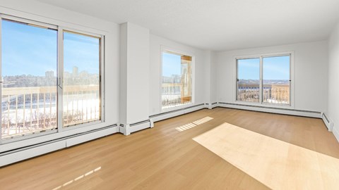 A large empty room with wooden floors and windows overlooking a parking lot.