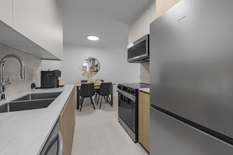 A modern kitchen with a stainless steel refrigerator, sink, and dining table.