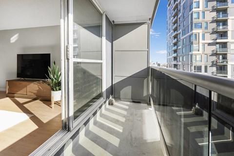 A modern balcony with glass railings and a flat screen TV in the living room.