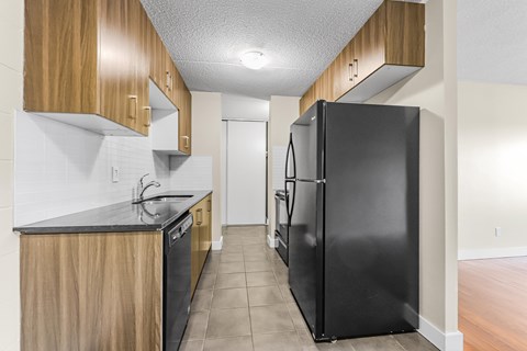 A black refrigerator sits in a kitchen with wooden cabinets.