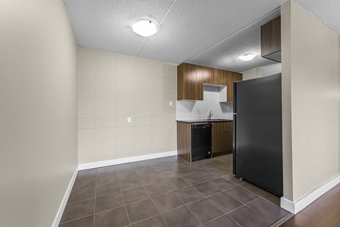 A kitchen area with a black refrigerator and a black trash can.