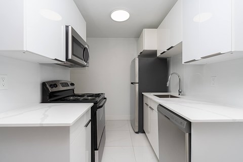 A white kitchen with black appliances and a white counter top.