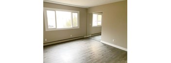 A room with light wood flooring and two windows.