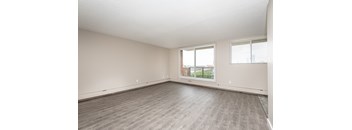 A spacious room with a large window and wooden flooring.