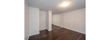 A room with white walls and wooden flooring with a door on the left and a mirror on the right.