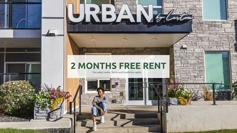 A person is sitting on the steps of a building with a sign that reads "URBAN 2 MONTHS FREE RENT".