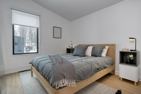 A bedroom with a bed, nightstand, and window at The Grove Apartments, Ontario