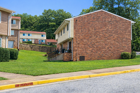 A brick building with a white trimmed window sits in front of a green lawn.