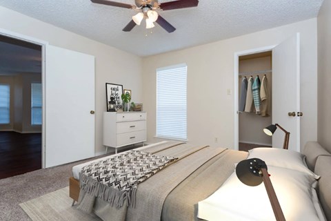 A bedroom with a bed, a couch, a ceiling fan, and a window with blinds.