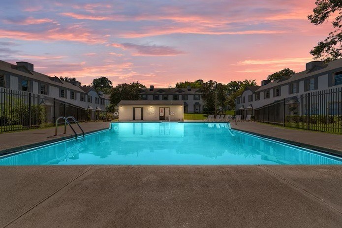 A swimming pool in front of a building with a sunset in the background.
