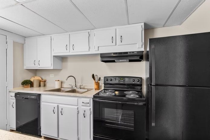 A black refrigerator is on the right side of a kitchen with white cabinets.