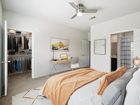 A bedroom with a bed, a desk, a chair, a closet, and a ceiling fan.
