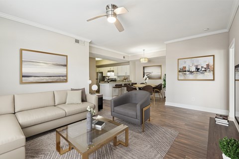 A living room with a beige couch, a grey armchair, a glass coffee table, and a ceiling fan.
