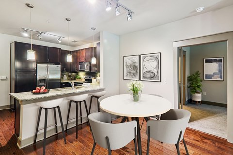 A kitchen with a table and chairs in the foreground and a framed picture on the wall.