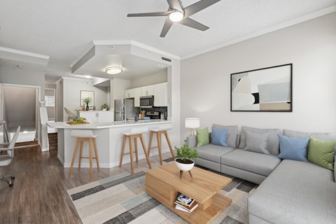 A modern living room with a grey couch, a wooden coffee table, and a kitchen area in the background.